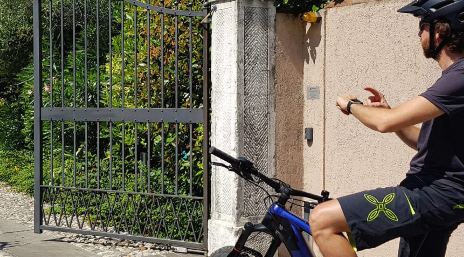 Cycliste qui ouvre un portail battant en fer forgé depuis sa montre connectée, sans télécommande